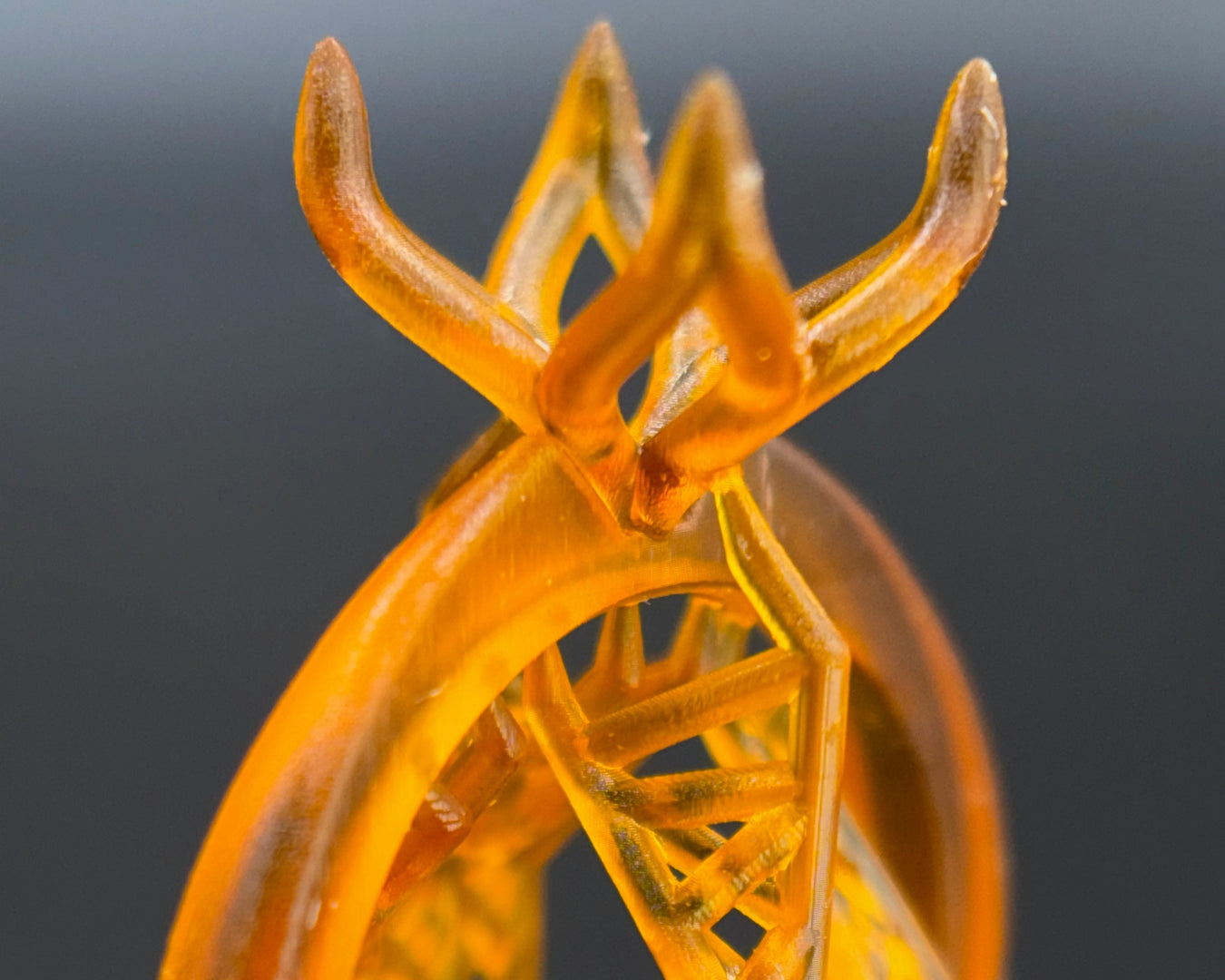 Close-up of a translucent like orange 3D printed ring part for direct investment jewelry casting, made with EmberCast Px resin with a complex, branching crown-like top and visible internal support structure, photographed against a dark gray background.

